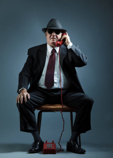 elegant senior man speaking on a vintage phone old mafia hitman answering a phone call mafia boss stock pictures, royalty-free photos & images