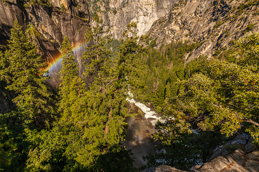 Nature spectacle of powerful flowing river into a valley with a rainbow. Vernal Falls trail, Yosemite Valley National Park during peak snowmelt 2023, California, USA.