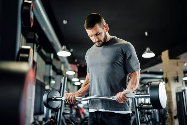 istock Muscular man working out in gym doing bicep exercises with barbell 1562297470