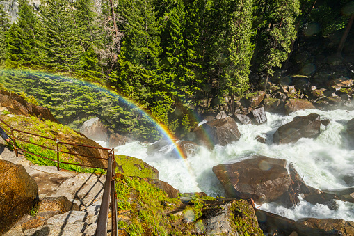 Nature spectacle of powerful flowing river into a valley with a rainbow. Vernal Falls trail, Yosemite Valley National Park during peak snowmelt 2023, California, USA.