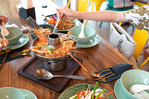 Female hand with chopsticks reaching for Thai Tom Yum Gong soup with seafood and vegetables in a restaurant closeup. Classical Thai food artistically served in a restaurant