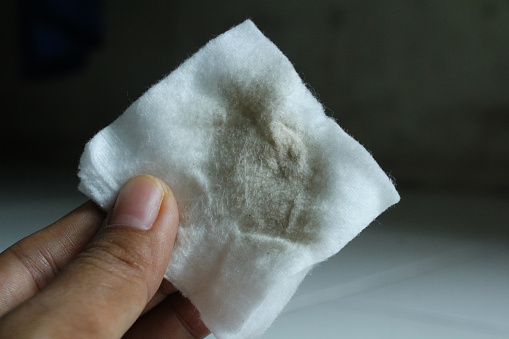 a woman's hand holding a dirty cotton swab used to clean her face