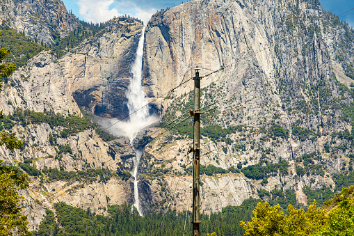 Power lines and Yosemite Falls at peak flow on a sunny summer day in 2023, Yosemite Valley, National Park, California, USA.