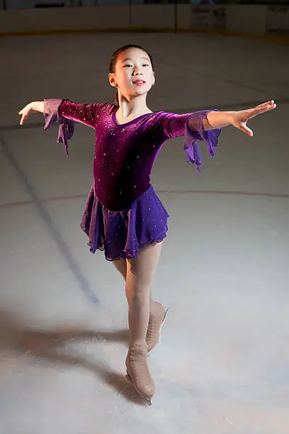 A young female asian figure skater with arms out shot on the ice.