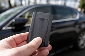 Hand of man holding remote control car key, next to a black vehicle. Smart card for cars with keyless entry system.