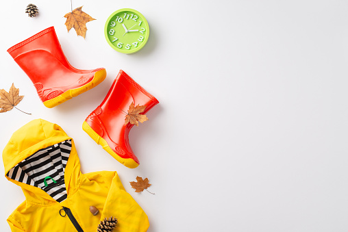 Enthralling autumn rain experience for children. Frame a top view picture exhibiting a bright yellow raincoat and gumboots on a white isolated background, inviting text or advert incorporation