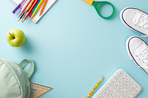 Embrace the power of technology in your studies. An overhead shot captures a rucksack, sneakers, a keyboard and stationery on serene pastel blue backdrop, empty frame perfect for educational content