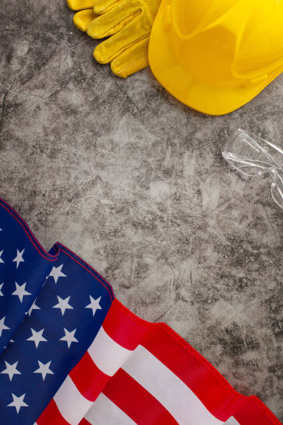 istock Honoring the hard work of construction workers on Labor Day. Top-down image showcasing american flag, yellow helmet and work gloves on grunge textured grey concrete. Suitable for ads or text 1562414686