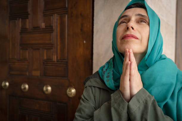 Pray and bible concept. Hand in hand together on bible by senior woman (worship christian), thinking and closed her eyes at church. Person side view, female praying and hope for peace-vertical image.