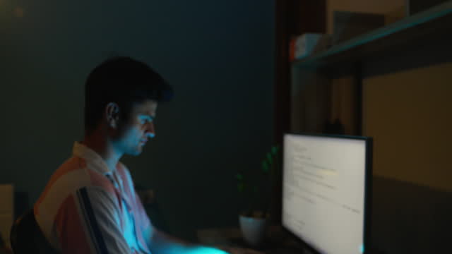 Focused Indian young man working seriously over computer in home office late at night