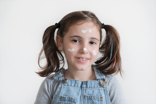 Little girl applying cream on her face