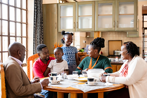 Waist-up view of 6 and 9 year old children, parents in 20s and 30s, and grandparents in early 60s sitting together in sunny dining room.