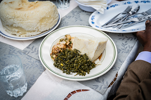 Plate filled with chicken stew, managu, a leafy green vegetable side dish, and ugali, a corn flour cake.