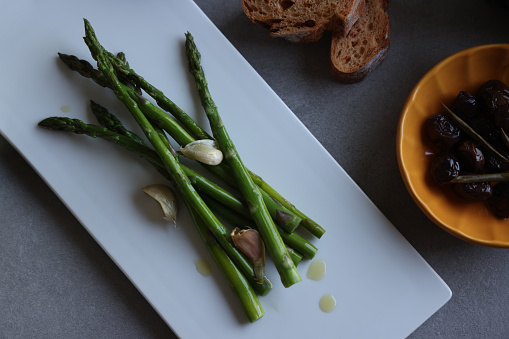 Fresh green asparagus on white plate with olive and bread