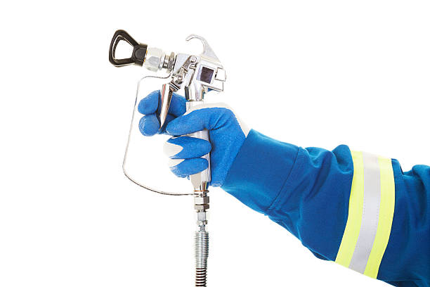 Airless Spray Gun A painter's arm and hand in safety coveralls and gloves holding an Industrial size airless spray gun used for industrial painting and coating.  Shot on white background. airless stock pictures, royalty-free photos & images