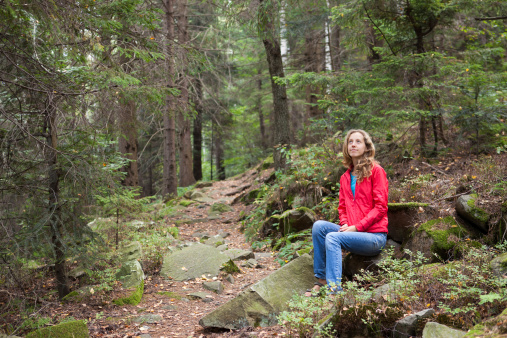 Young hiker woman sitting on a halt in stones among the forest. Hiking in the mountains rise on a forest footpath