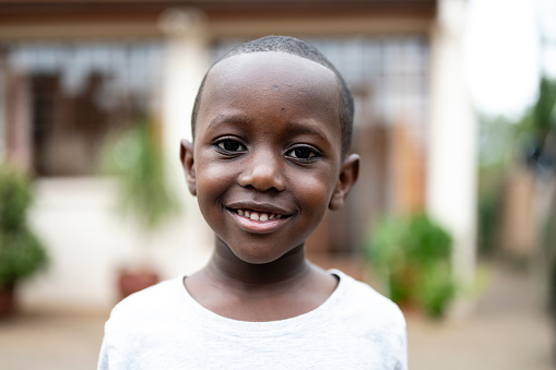 Close view of 6 year old child wearing white t-shirt with round neckline and looking at camera with contented smile.