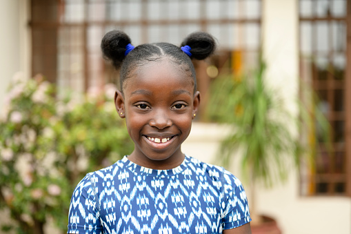 Young child with hair styled up and in two buns wearing blue and white patterned top and smiling at camera.