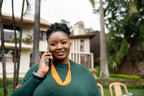 Close candid view of young woman with hair in braided up-do, wearing green garment with colorful jewelry, smiling and looking away while conversing with caller.