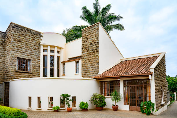 Mix of brick and stucco, paned glass, low-pitched tile roof with paved path and landscaping. Residential property in Africa.