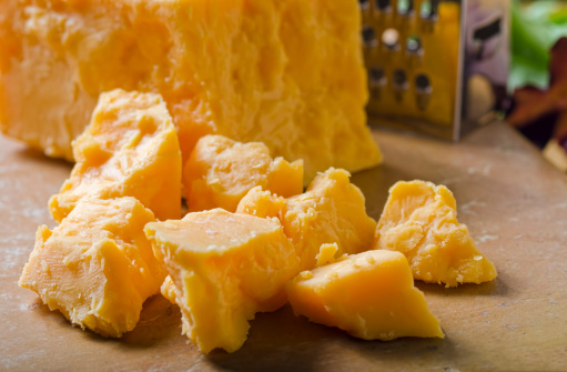 Chunks of aged cheddar cheese with grater.