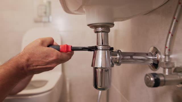 The plumber's hands using the wrench to fix the sink