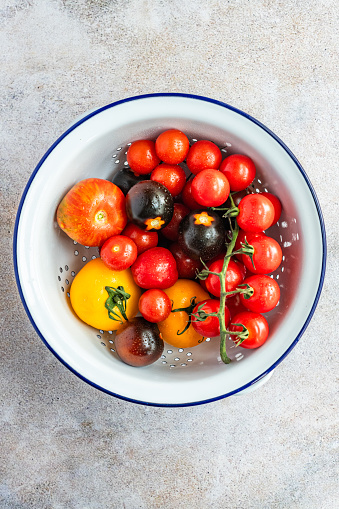 Various types of whole organic tomatoes in a white enamel colander