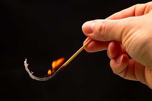 Fire and smoke. Burning match in hand on a black background. Heat and light from fire flame