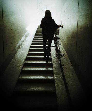 A Japanese woman pushing her bicycle up the steps from an indoor bicycle parking area in Tokyo, Japan.