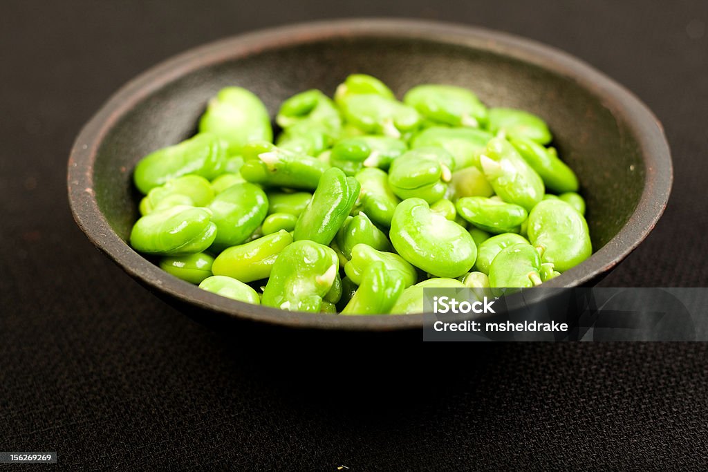 Fava Beans Freshly shelled fava beans on black textured cloth in black bowl Bean Stock Photo