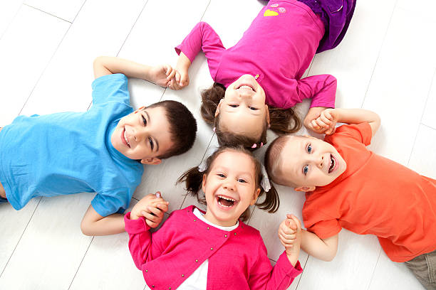 Happy kids lying face up in a circle on the floor smiling stock photo