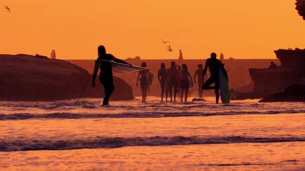 silhuetas de surfistas caminhando na costa do oceano atlântico ao pôr do sol em marrocos - wave curl - fotografias e filmes do acervo