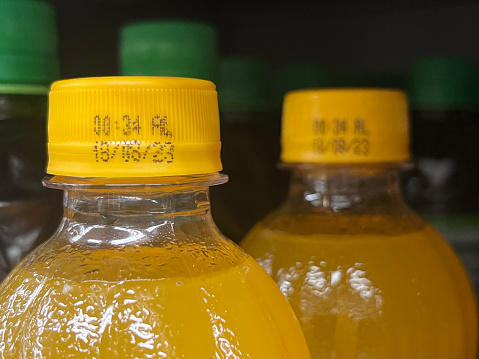 Two bottles of orange juice. Closeup image of expiry date on bottle cap.