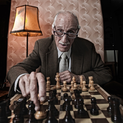 One old man playing chess in his humble living room. More files of this model and series on port. Made with professional equipment. Square format in shallow depth of field.