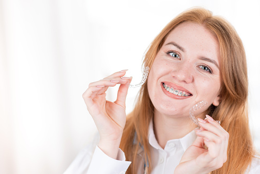 Dental care.Smiling girl with red hair making heart shape from teeth aligners