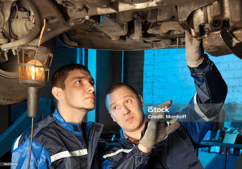 Dos mecánicos trabajando bajo auto en tienda de reparaciones - Foto de stock de Adulto libre de derechos