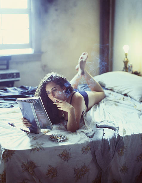 Young Woman Smoking and Reading Magazine on Bed stock photo
