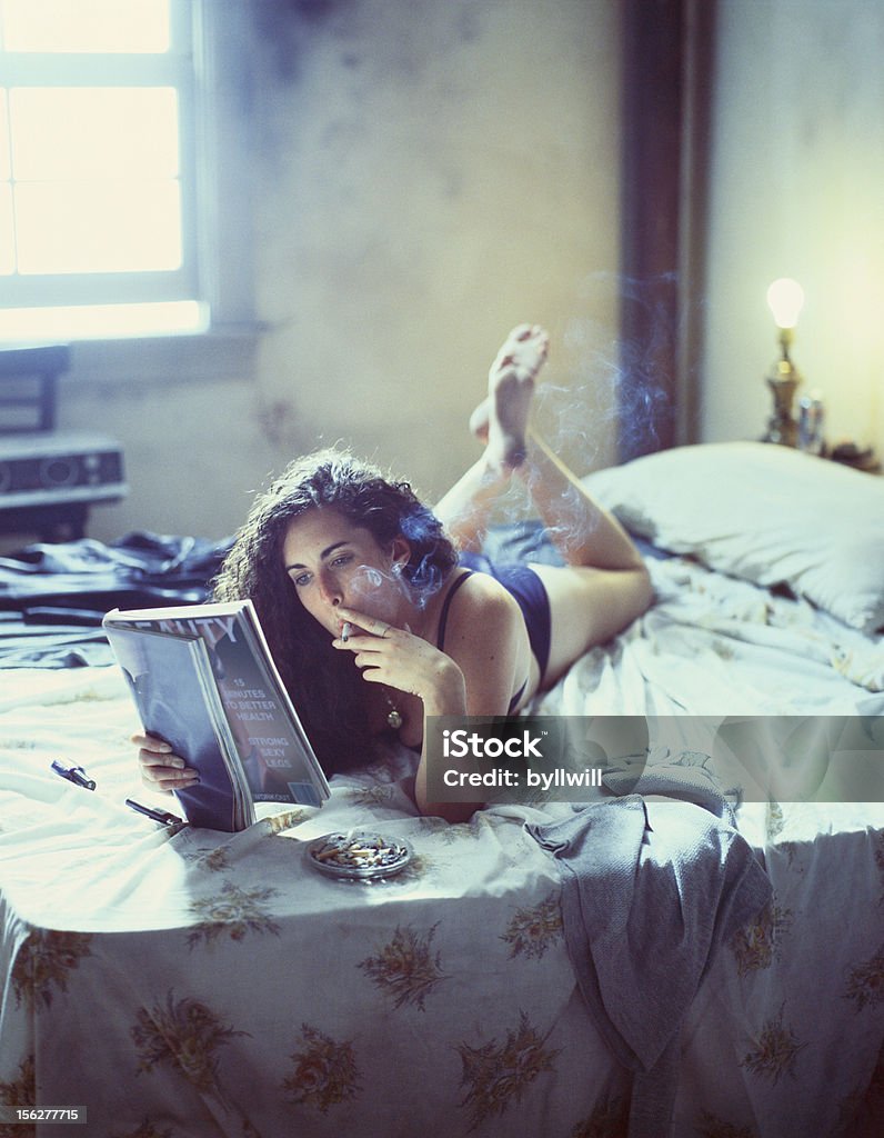 Jovem mulher fumantes e a revista de leitura na cama - Foto de stock de Cama royalty-free