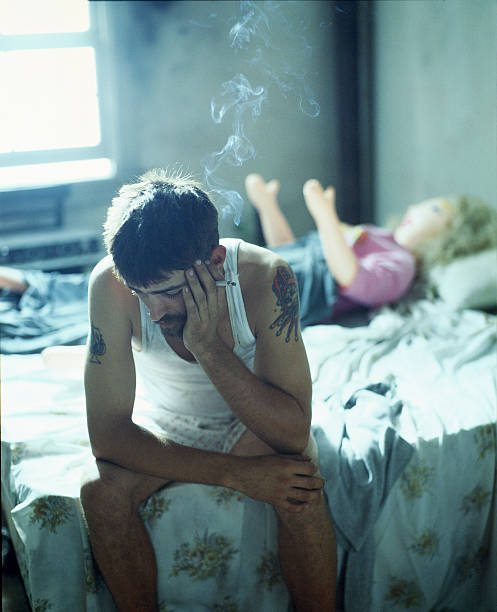 Man Smoking on Bed with Blow Up Doll in Background stock photo