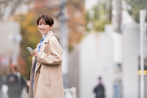 An asian woman is walking in the city. She is wearing a coat.