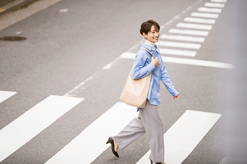 A Japanese woman is crossing a pedestrian crossing. She wears smart casual clothes.