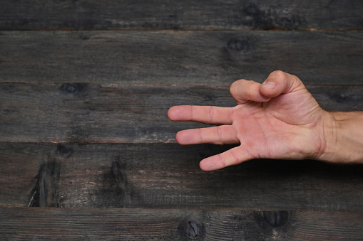 Hand of man showing fingers on wooden background counting number 3 showing three fingers.