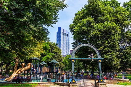Boston, Massachusetts, USA - July 19, 2023: The Tadpole Playground is next to the Frog Pond on the Boston Common, and provides art, water features & entertainment for the whole family. The Tadpole Playground opened in 2002. Boston downtown district buildings in the background.