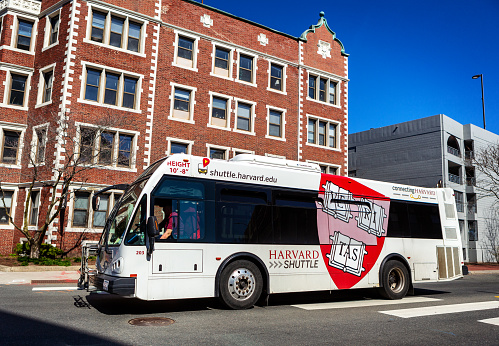 Cambridge, Massachusetts, USA - April 10, 2023: A white Harvard University Shuttle Bus. The Harvard Veritas logo is on the side of the bus. The Harvard Shuttle buses serve the Cambridge and Allston (Boston) campuses.