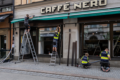 Stockholm, Sweden June 20, 2023 Four workmen replace the aluminum siding and window frames on a restaurant exterior.