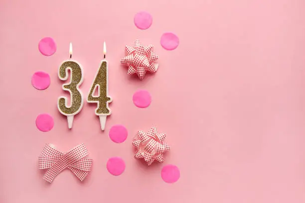 Number 34 on pastel pink background with festive decor. Happy birthday candles. The concept of celebrating a birthday, anniversary, important date, holiday. Copy space. Banner