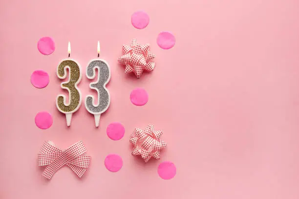 Number 33 on pastel pink background with festive decor. Happy birthday candles. The concept of celebrating a birthday, anniversary, important date, holiday. Copy space. Banner