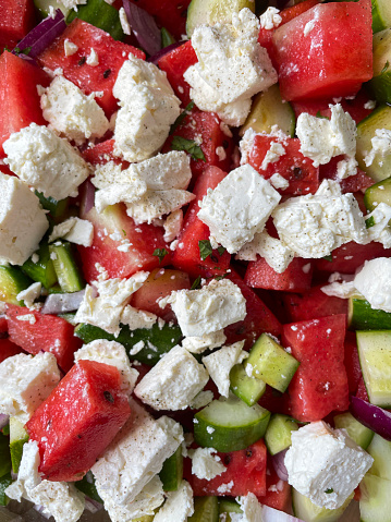 Stock photo showing a close-up, elevated view of healthy eating image of a salad bowl containing a watermelon salad with red onion, cucumber, black olives, feta cheese and mint leaves.