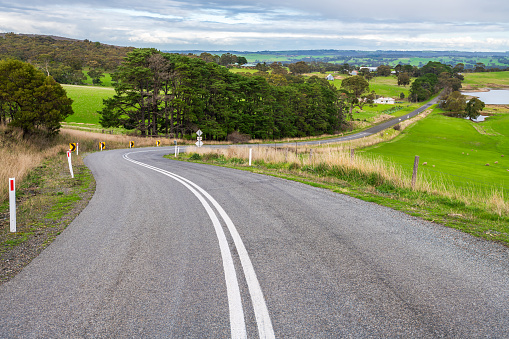 Plain asphalt road curve through Adelaide Hills farmlands during winter season, South Australia