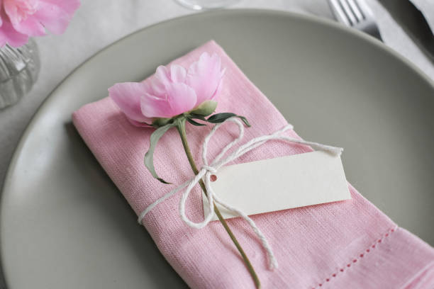Mockup blank card for greeting or guest's name on the plate. Table setting with light green ceramic plates and pink peonies
